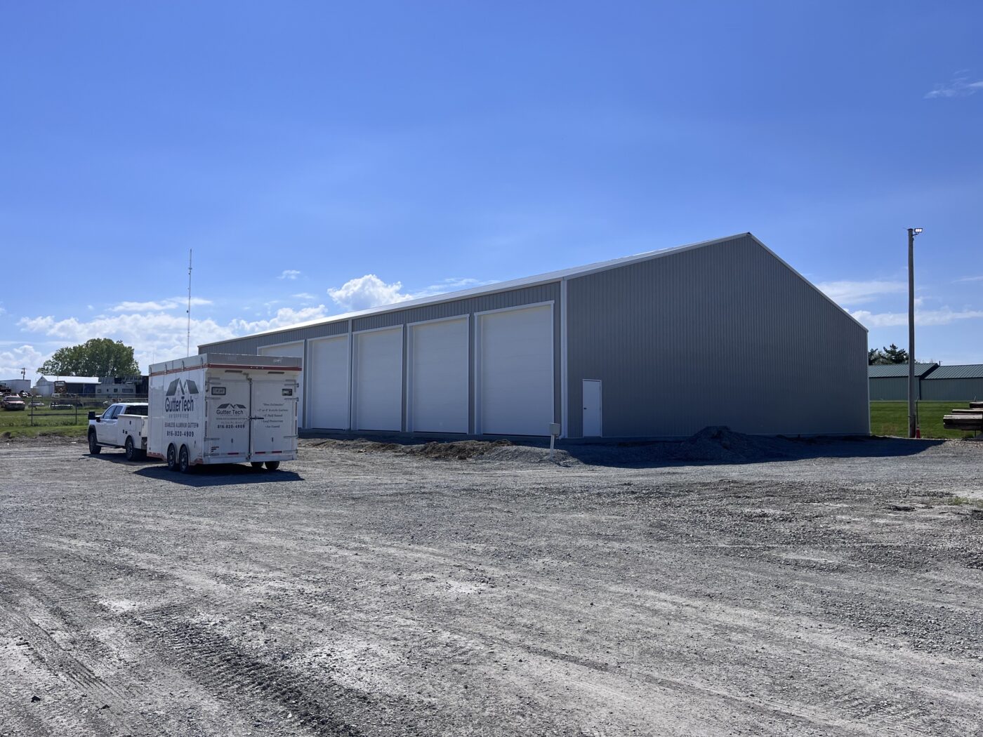 Large gray metal building with white seamless gutters installed in Cameron, Missouri, Gutter Tech trailer parked nearby.