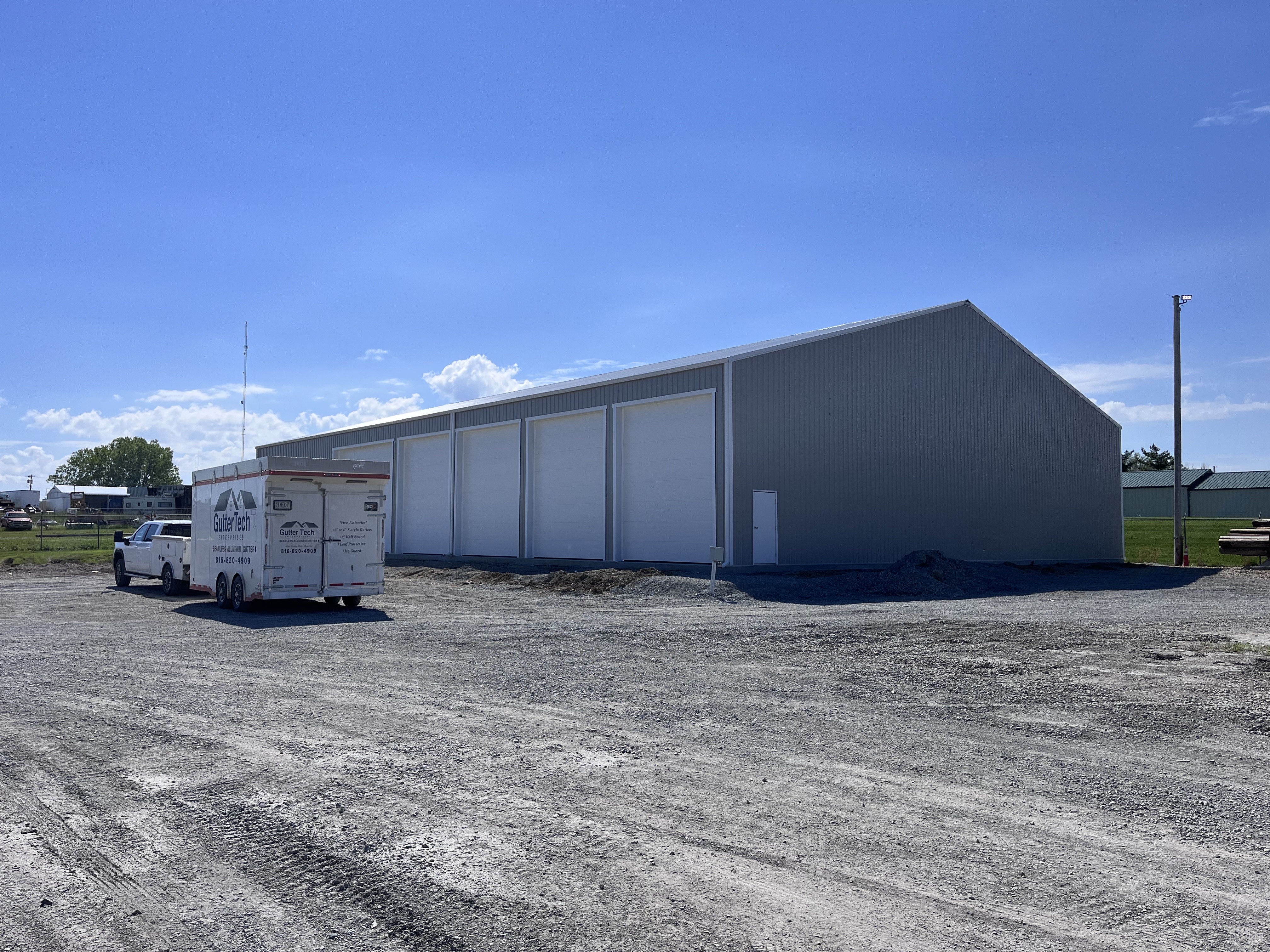 Large gray metal building with white seamless gutters installed in Cameron, Missouri, Gutter Tech trailer parked nearby.