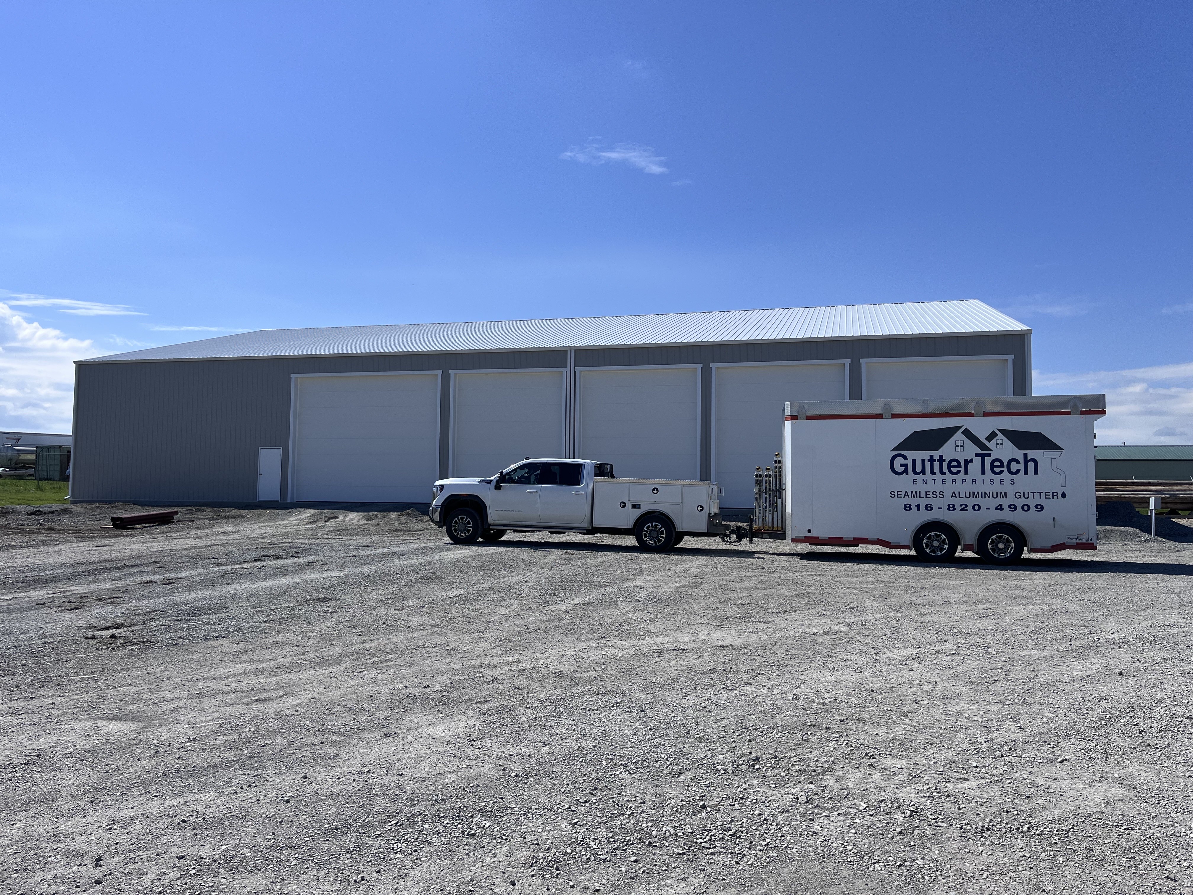 Side view of a commercial metal building featuring newly installed 6-inch white seamless gutters to manage runoff from the expansive roof.
