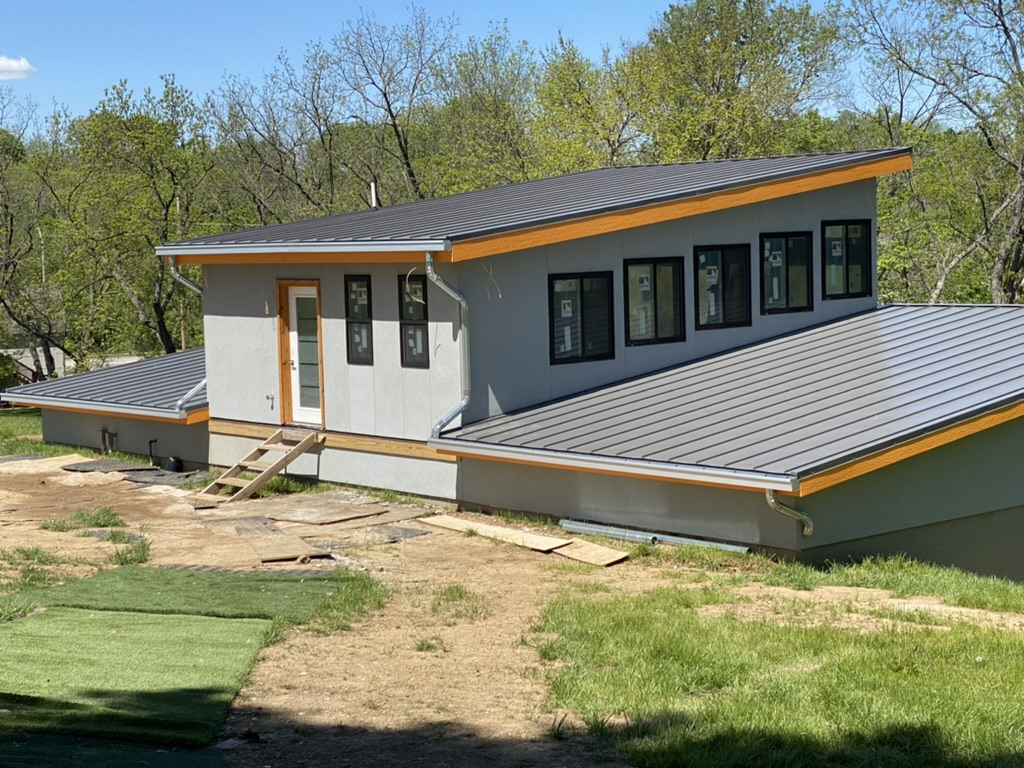Top view of gray modern building with sloped roof and black framed windows - Gray gutter with aluminum downspouts to