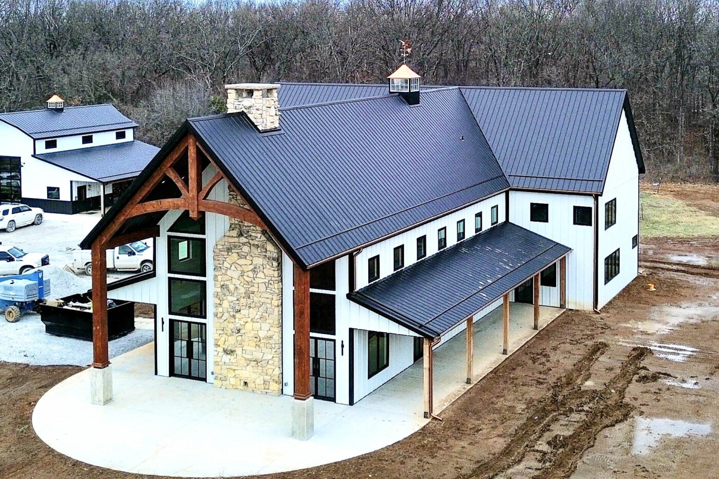 Side angle of the home showing multiple copper downspouts and half-round gutters installed on a white and stone-clad exterior, set against bare ground and vehicles.