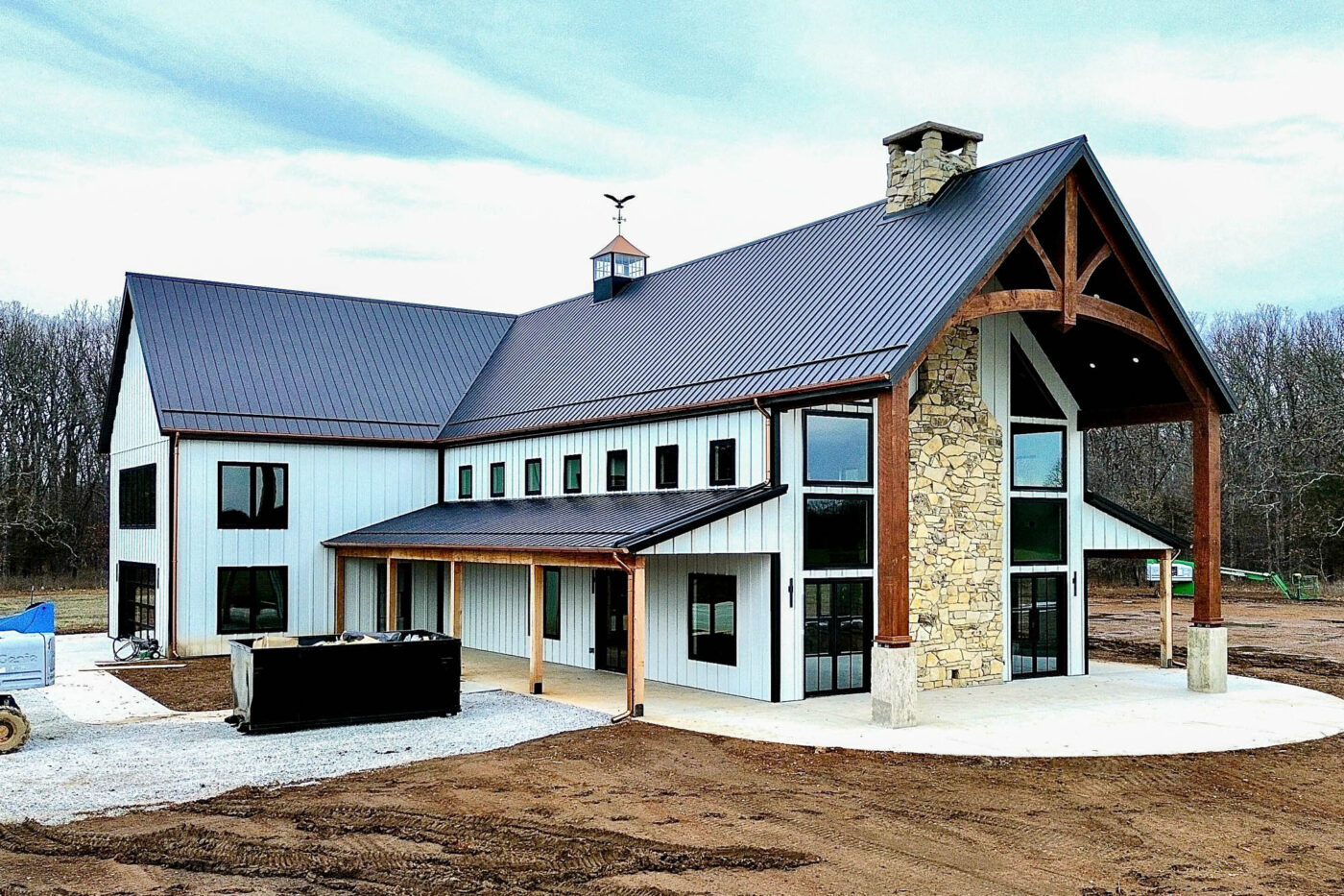 Angled front view of a newly constructed home with black roofing and copper half-round gutters, featuring large windows, stone accents, and round downspouts.