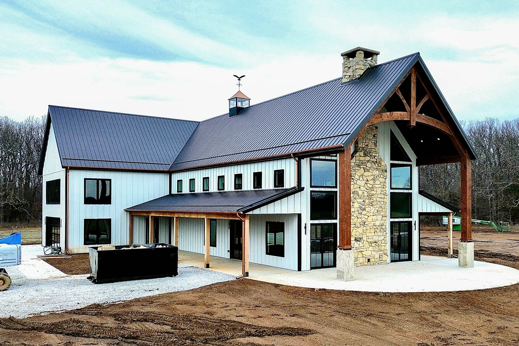 Angled front view of a newly constructed home with black roofing and copper half-round gutters, featuring large windows, stone accents, and round downspouts.