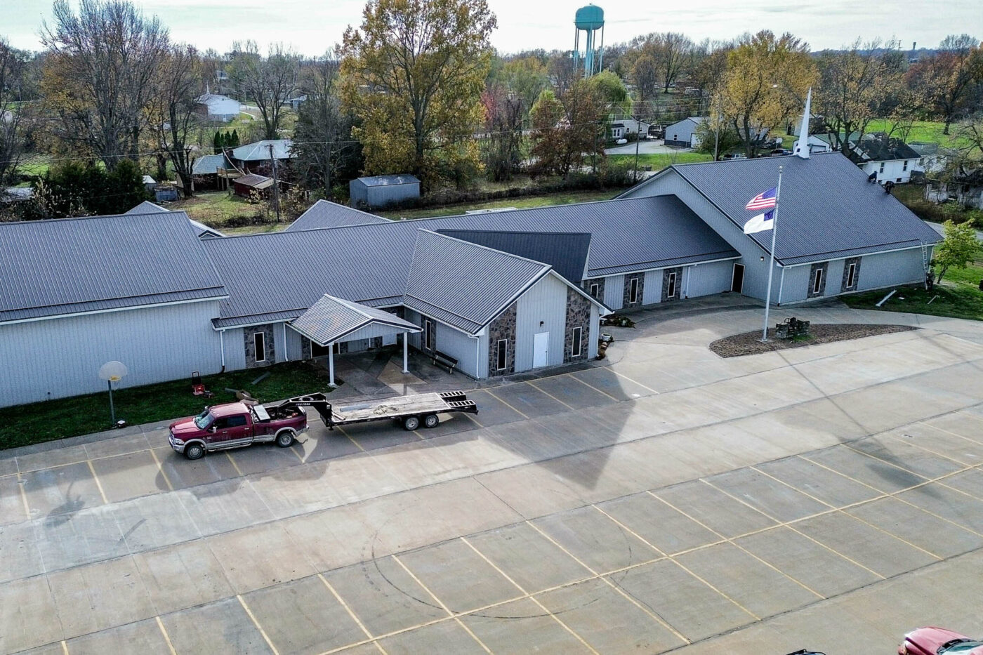 Aerial view of a church with a large parking lot, featuring new gutter systems installed along the dark metal roofline and light-colored exterior walls.