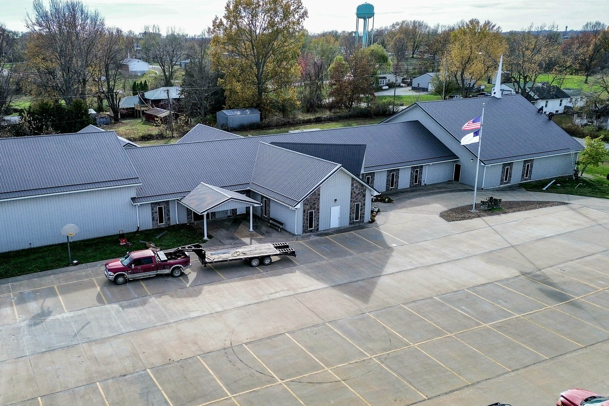 Aerial view of a church with a large parking lot, featuring new gutter systems installed along the dark metal roofline and light-colored exterior walls.