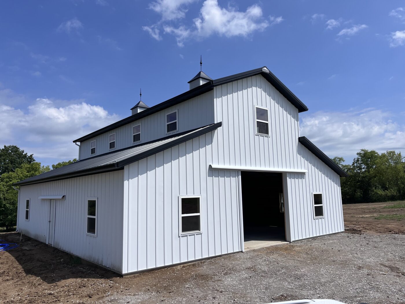 Large white metal building with 6-inch black gutters and white 3×4 downspouts installed by Gutter Tech in Kearney, Missouri.