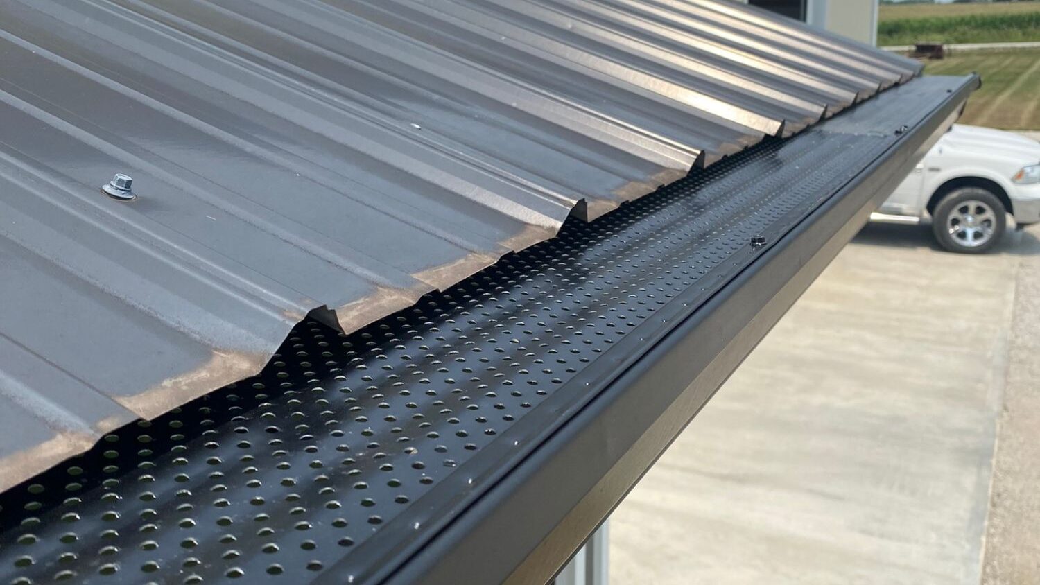 Close-up view of a perforated gutter guard installed under a metal roof. Just one of many rain gutter options at Gutter Tech.