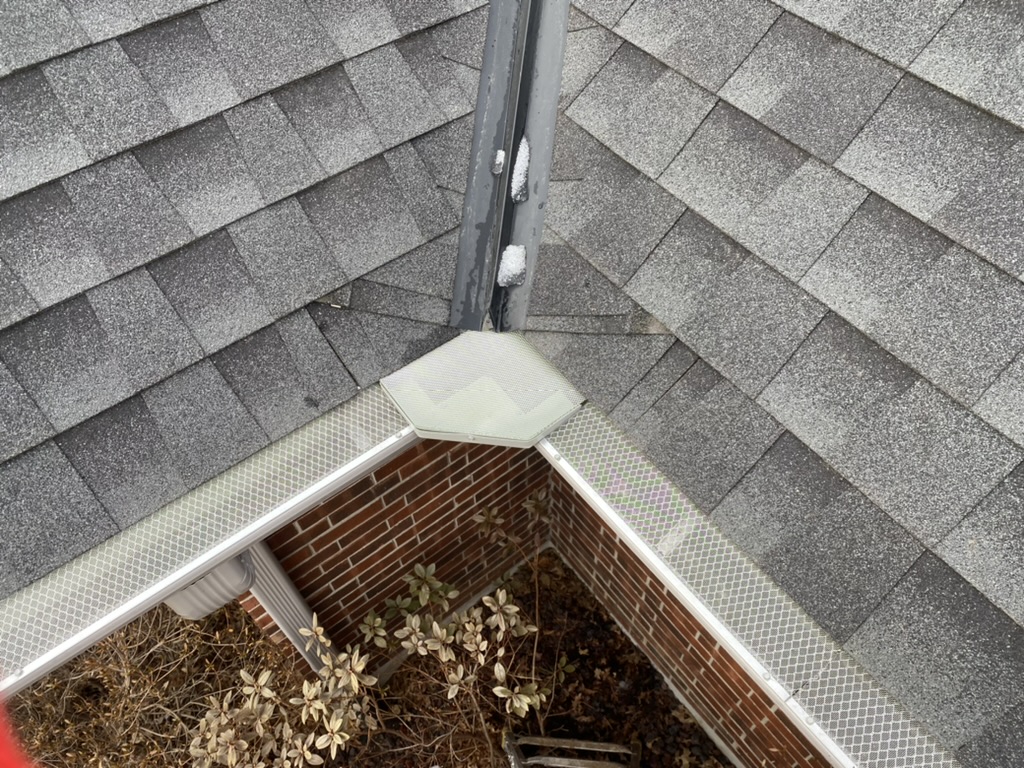 Top view of white gutter with metal mesh gutter guard installed on gray roof of red-brick house